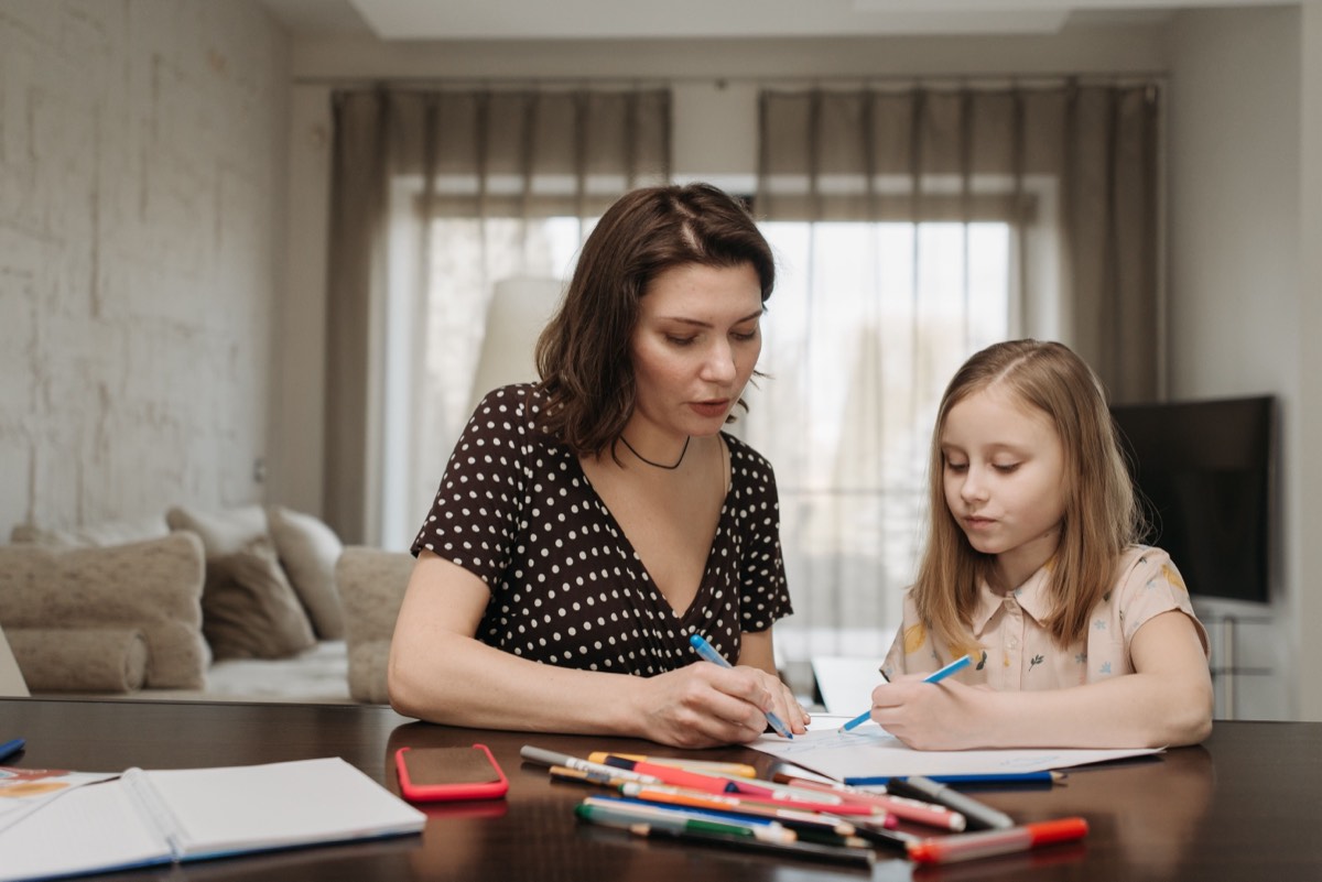 A mom helping her daughter with a writing lesson at the table.